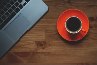 Photo of a coffee cup sitting next to a laptop