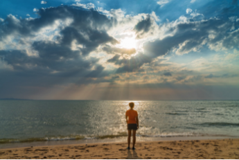 Photo of man standing on a beach looking at the sun