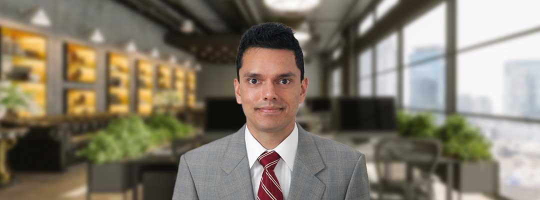 Headshot of Ameer Acharya wearing a gray suit and a red tie