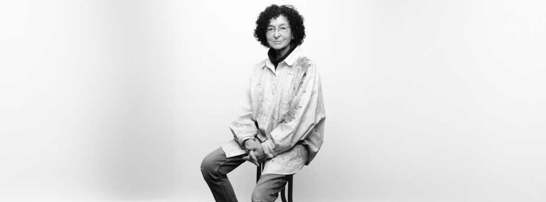 Photo of Elisabeth Koss sitting on a stool in front of a gray background