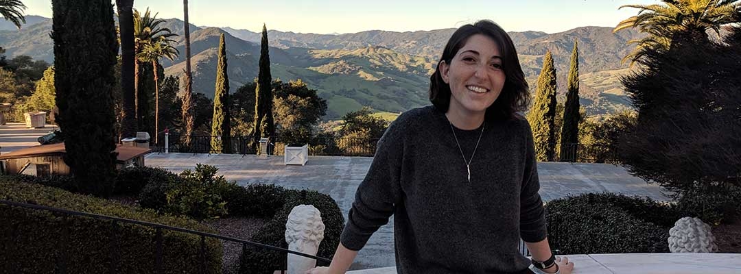 Emilie Biondi sitting on a stone bench in front of a hilly background at sunset