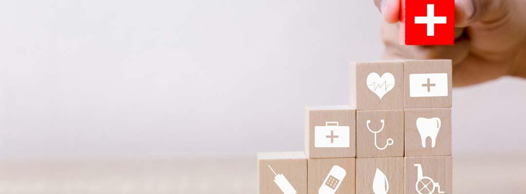 Hand stacking red block with white cross on stack of wooden blocks with medical logos