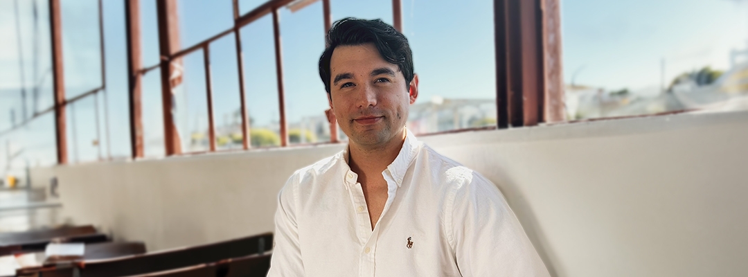 Photo of Isaac Stuart wearing a white button-down shirt in front of a glass window