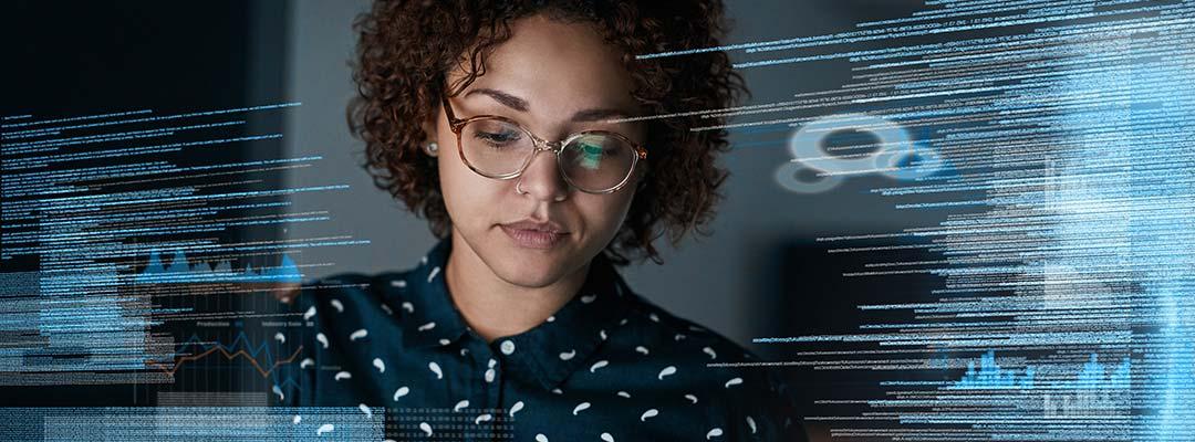 A woman with curly hair and glasses with a computer screen reflection surrounding her