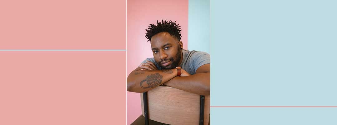 Photo of Reiss Reid sitting on a chair backward in front of a pink and blue background