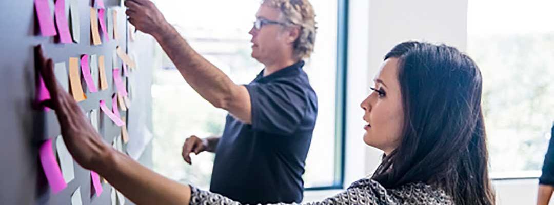 Photo of man and woman putting post-it notes on a blackboard