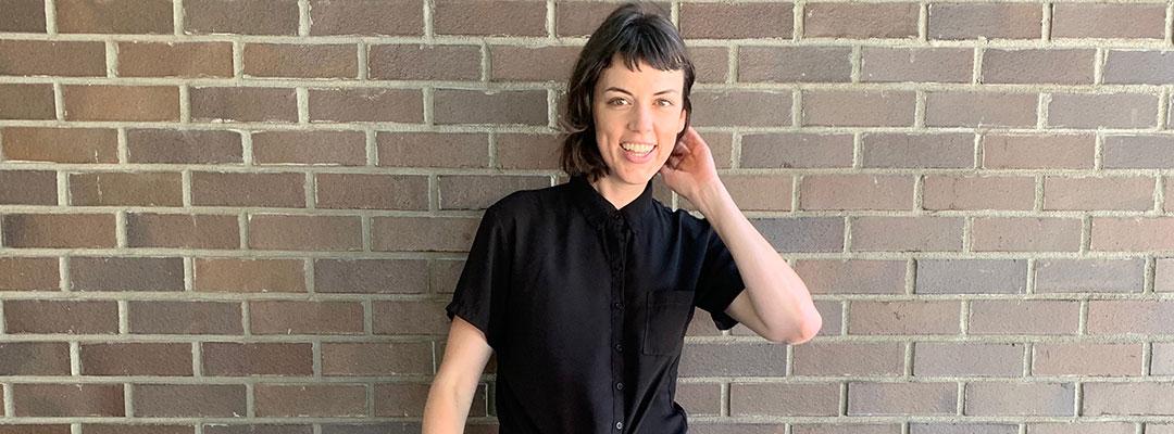 Professional Sequence in Editing gradaute Alison Kranz standing in front of a brick wall, hand brushing back hair by ear