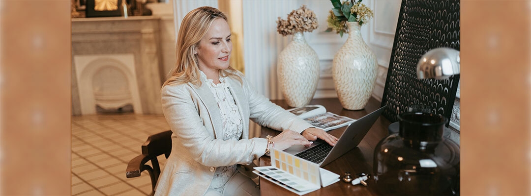 Certificate Program in Interior Design graduate Amber Lowi on laptop at desk with color palette