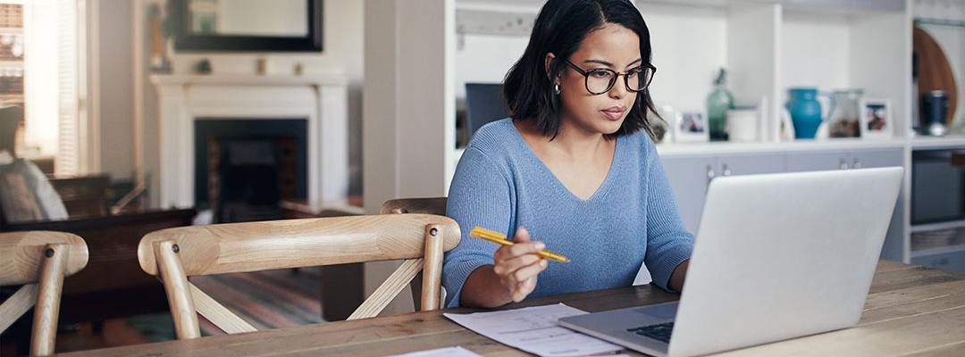 Woman sitting at kitchen table looking at laptop working on financial reports