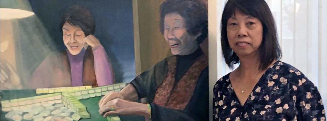 Certificate graduate Elinor Cheung in front of her painting depicting laughing Chinese women enjoying a game of mah-jongg