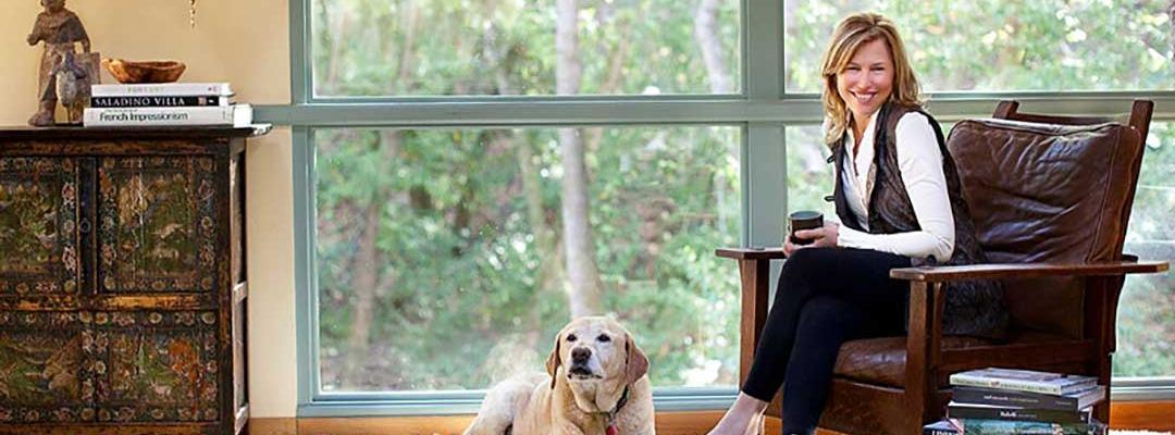 Photo of Llisa Staprans sitting on a leather chair with dog at her feet