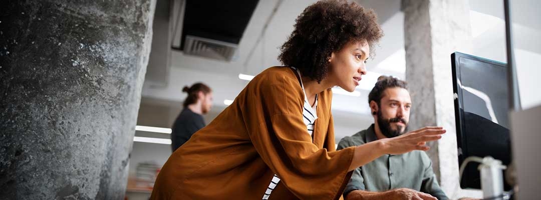 Black young adult woman points at a laptop in an office setting