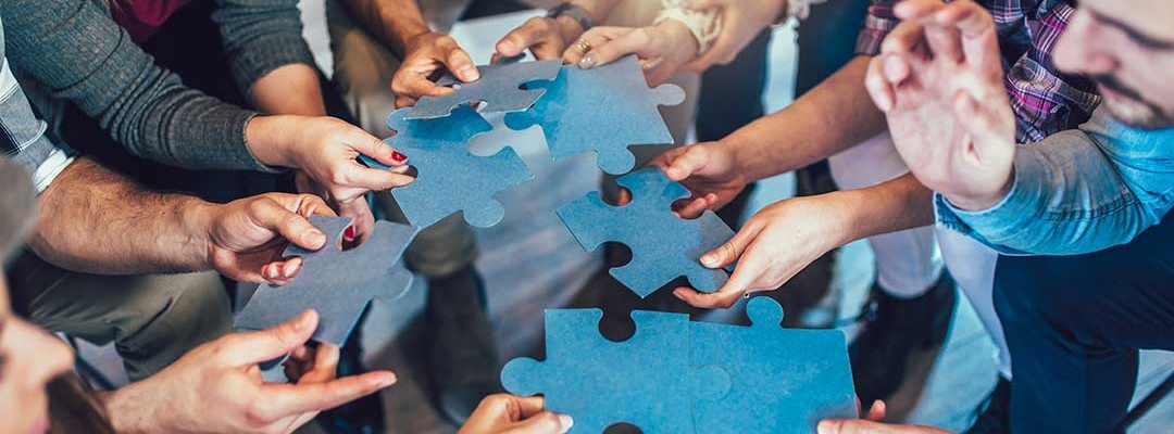 Multicultural employees putting together oversized jigsaw puzzle pieces