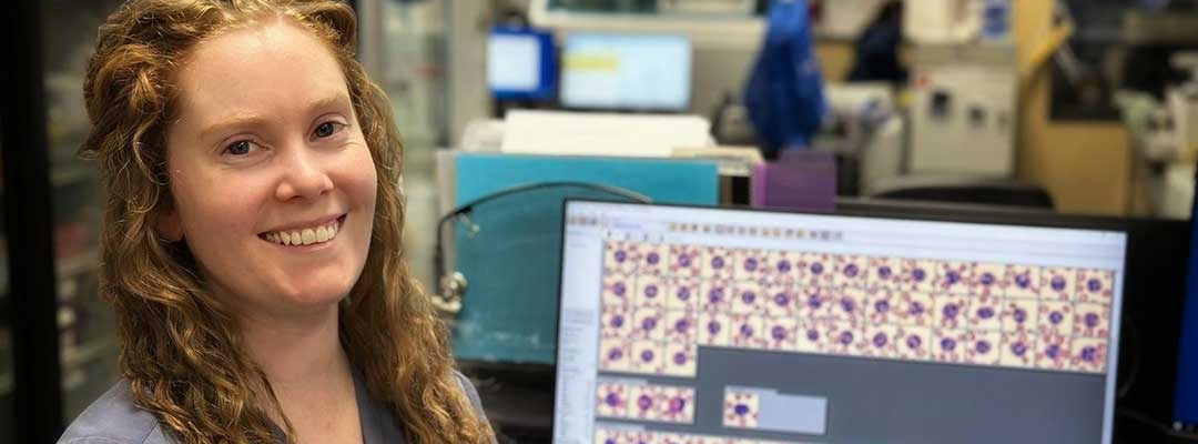 Photo of Gina LaMothe in the lab working on a laptop looking at blood samples