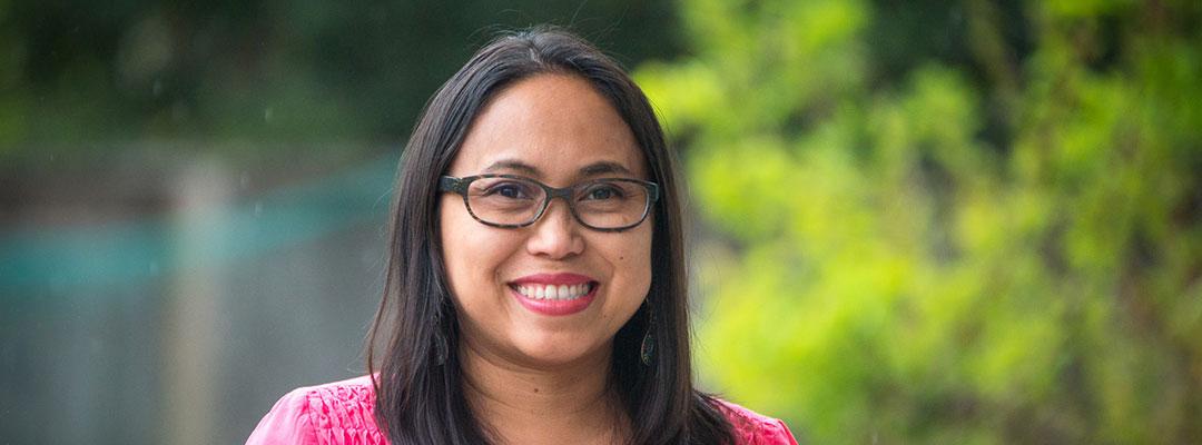 Project Management graduate Hazel Johanson, wearing glasses and smiling, outside with a green leafy background