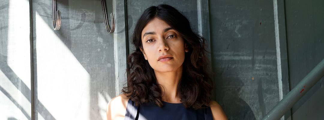 Post-Baccalaureate Health Professions Program graduate Jayinee Basu stands in front of a gray wall with sunlight on her shoulder