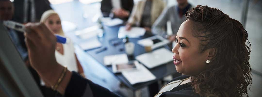 Black woman professional leading meeting while drawing on a white board