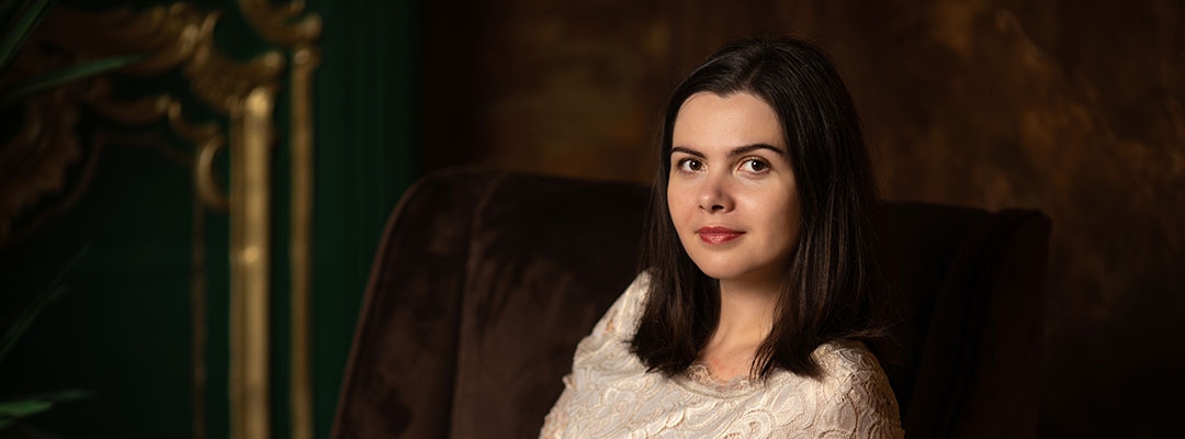 Photo of Polina Stepanova wearing a white dress while sitting in a brown suede chair