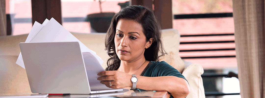 photo of woman studying papers while at an open laptop