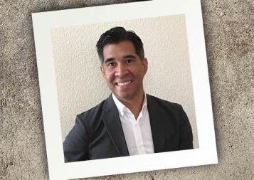 Square photograph on a granite surface at a tilt featuring College Admissions instructor Armando Diaz in an open-collar shirt and suit jacket