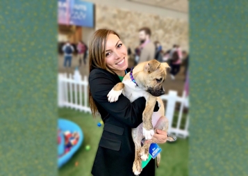 Marketing graduate Camille Rasmussen holding a puppy in front of a green background