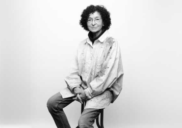 Photo of Elisabeth Koss sitting on a stool in front of a gray background