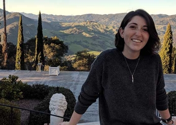 Emilie Biondi sitting on a stone bench in front of a hilly background at sunset