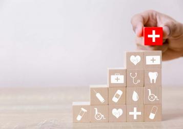 Hand stacking red block with white cross on stack of wooden blocks with medical logos