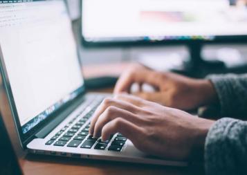 Hands typing on a blurred laptop screen