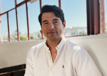 Photo of Isaac Stuart wearing a white button-down shirt in front of a glass window