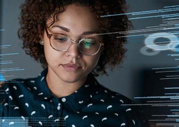 A woman with curly hair and glasses with a computer screen reflection surrounding her