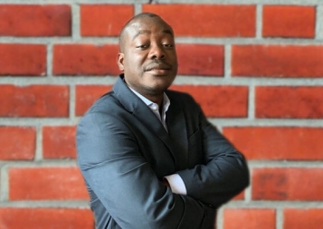 Headshot of Yves De Souza in front of a red-brick wall