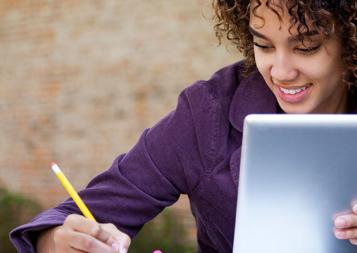 Black student learning on an tablet while taking notes on a notpad