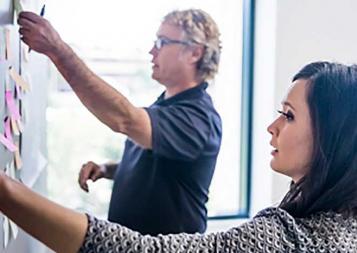 Photo of man and woman putting post-it notes on a blackboard