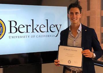 Photo of Alejandro Ruiz holding certificate of completion in front of a TV screen with Berkeley logo