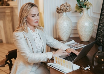 Certificate Program in Interior Design graduate Amber Lowi on laptop at desk with color palette