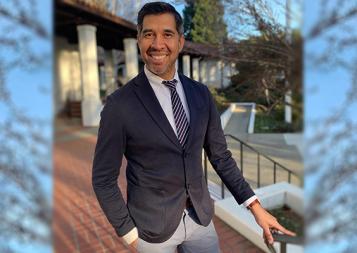 College Admissions and Career Planning certificate program instructor Armando Diaz in blazer and tie, standing next to railing with pillars in background. Photo.