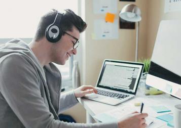 Student studying on a desk in front of a laptop and wearing headphones