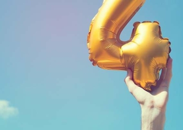 Image of hand holding a number 4 balloon against a blue sky