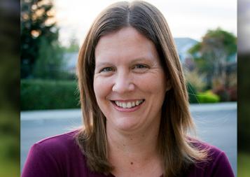 Headshot of Editing Honored Instructor Cathleen Small, standing outside with a neighborhood and sunset in background