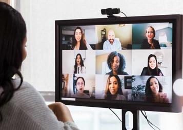 Photo of black young professional collaborating with team through online conferencing