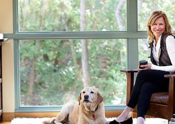 Photo of Llisa Staprans sitting on a leather chair with dog at her feet