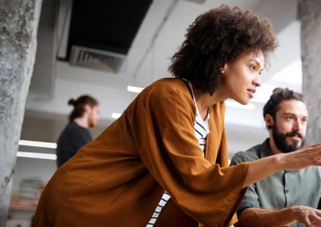 Black young adult woman points at a laptop in an office setting