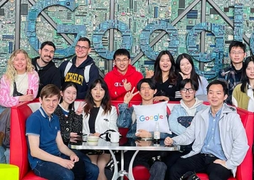 Group of international students sitting at a table in front of Google mosaic