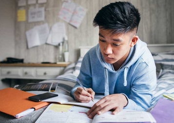 Photo of student lying on bed doing homework