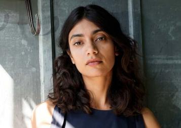 Post-Baccalaureate Health Professions Program graduate Jayinee Basu stands in front of a gray wall with sunlight on her shoulder