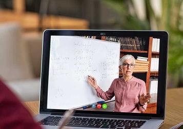 Photo of student looking at a laptop screen with instructor teaching on a whiteboard