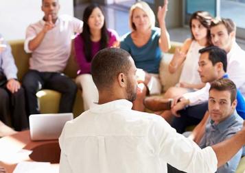 Image of young male professional standing up and presenting in front of colleagues