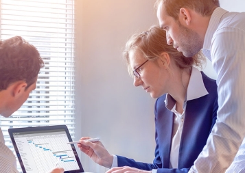 Three staff members gather around a laptop computer looking at a project chart