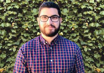 Graduate Raul Acosta stands in front of a wall covered in ivy